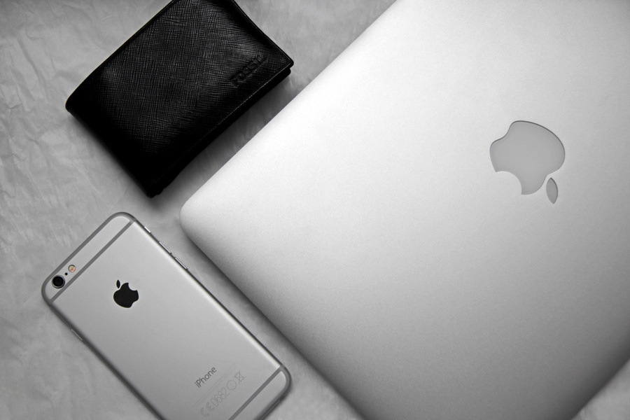 Gadgets, apple laptop, an iphone, and a wallet sit on a table